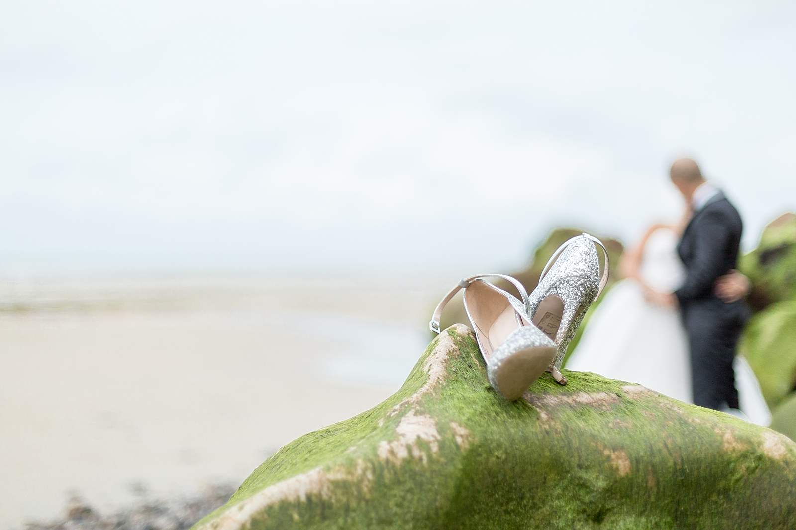 détails de mariage. les chaussures de la mariée sur un rocher a marée basse. les jeunes mariés s'embrassent en arrière plan