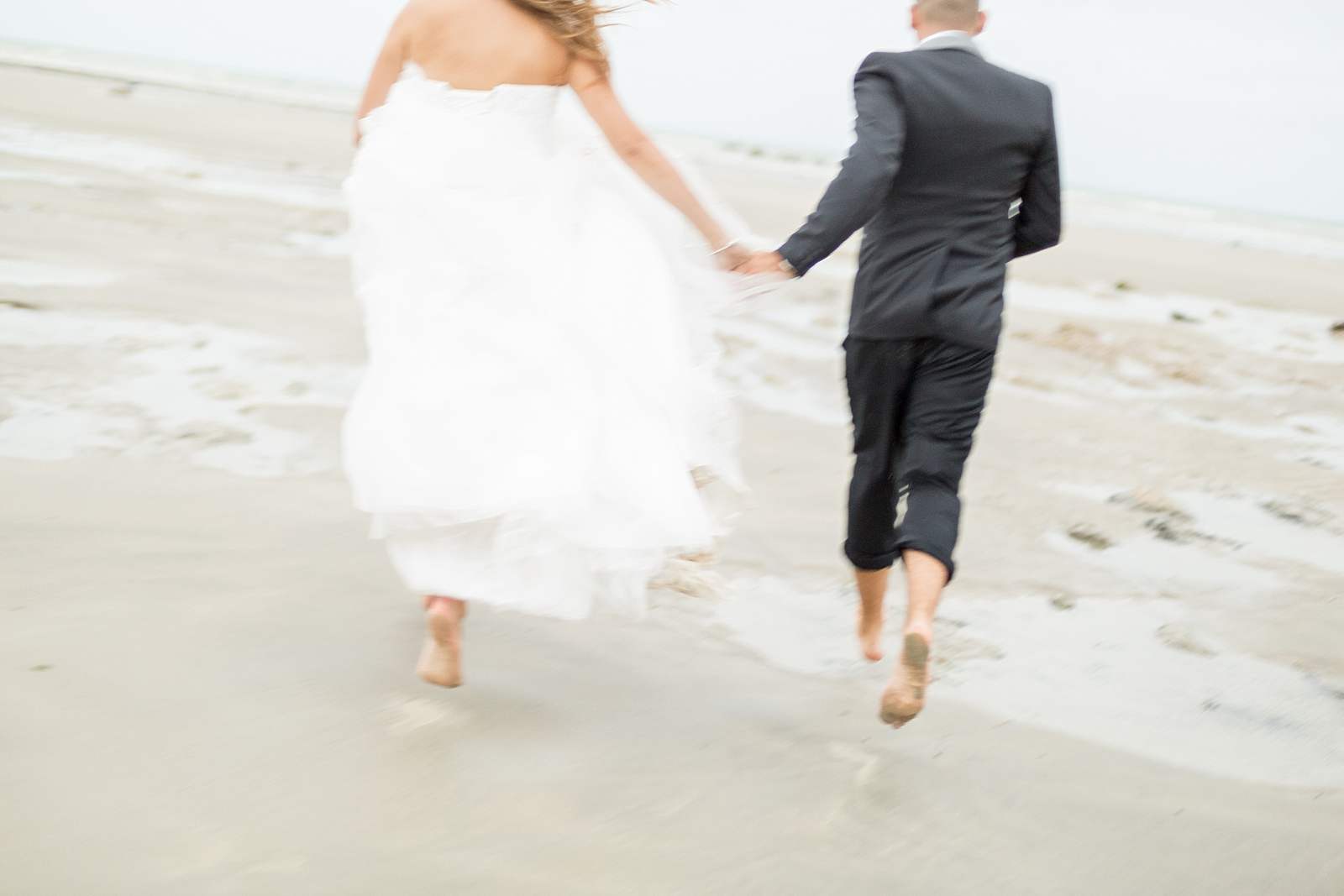 les mariés courent sur la plage main dans la main lors de la séance photo de couple en normandie.