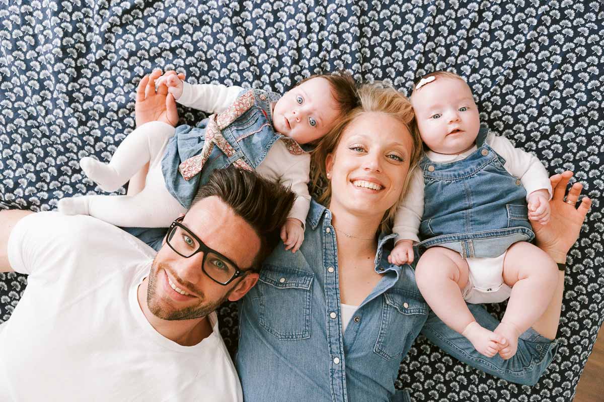 Portrait de famille en séance photo lifestyle. Parent et Jumelles allongés dans le lit parental